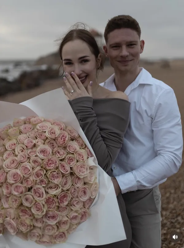 daria showing her engagement ring, with her fiancé, on a beach in porto